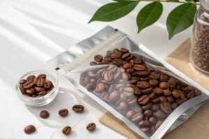Clear front zipper pouch filled with roasted coffee beans, placed on a white table with natural lighting.