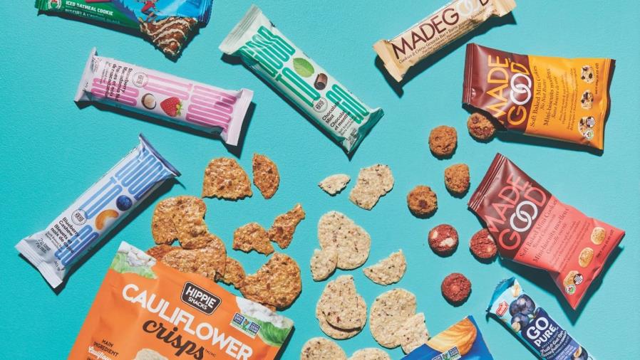 Assorted healthy snack bars and crispy chips in colorful packaging arranged on bright blue background.