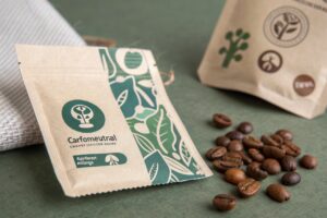 Sustainable kraft coffee pouch with green print design and coffee beans on green background.