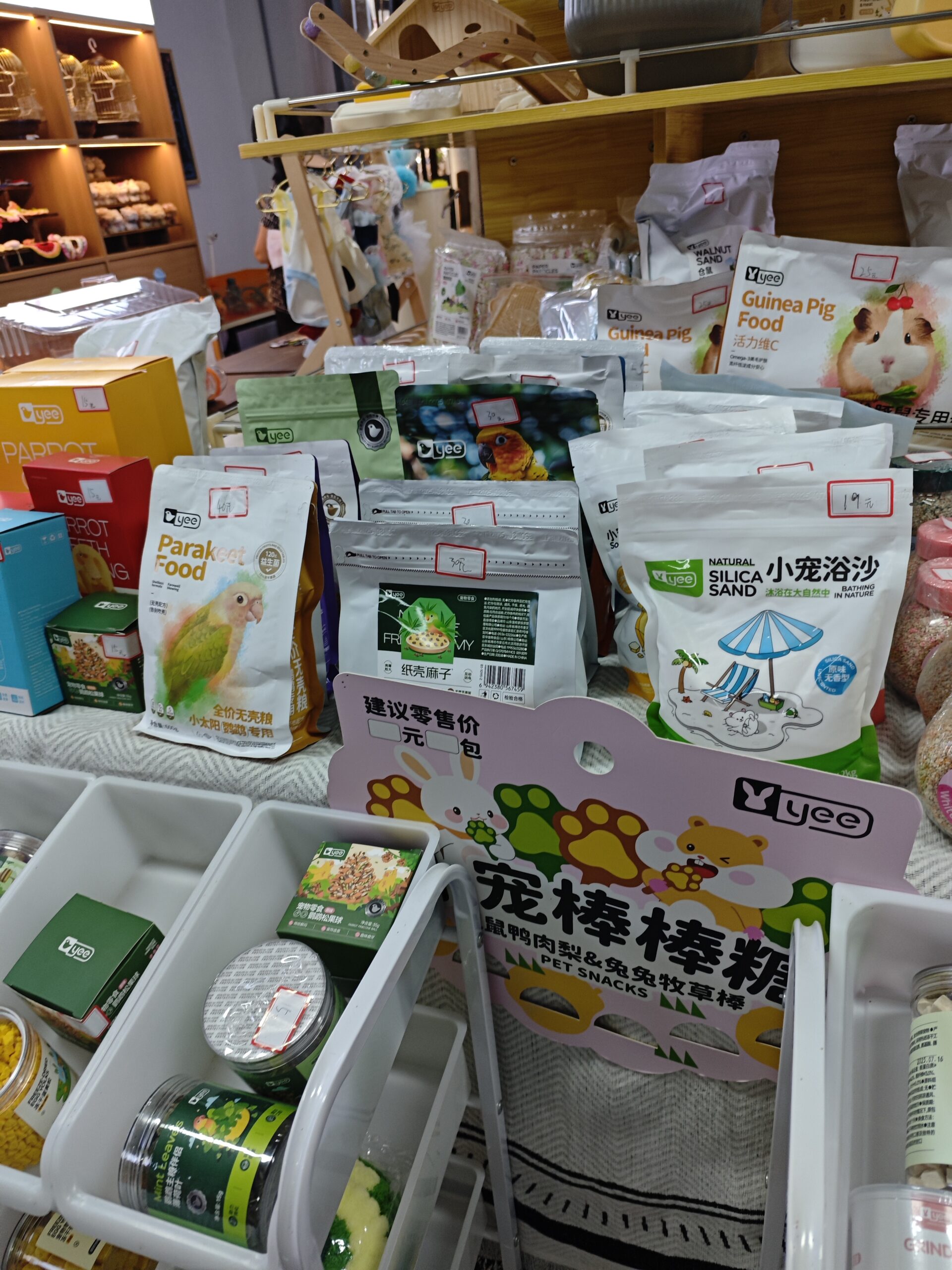 Assorted small pet food and snack packaging on display, including bird, guinea pig, and rabbit products.