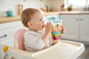 Baby holding BPA-free resealable organic food pouch in high chair.