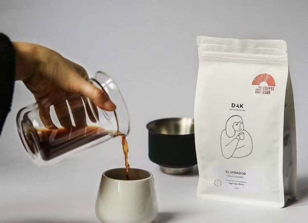 Hand pouring brewed coffee into cup beside minimalistic coffee bean packaging labeled