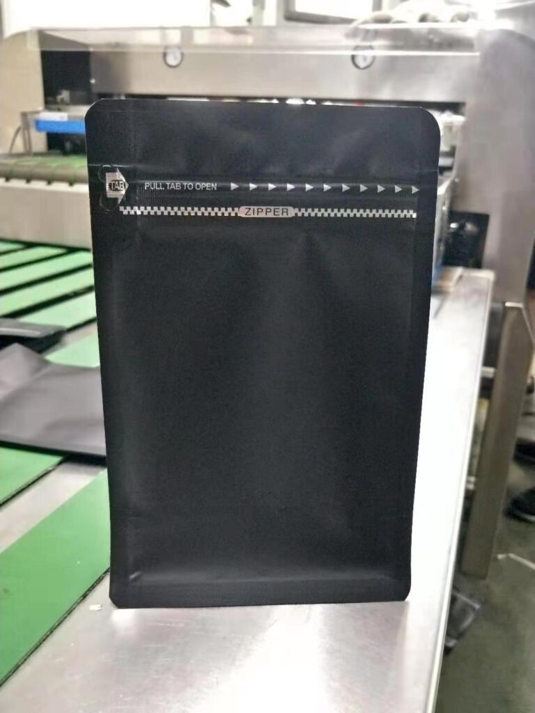 Matte black stand-up pouch with zipper and tear tab, placed on production line.