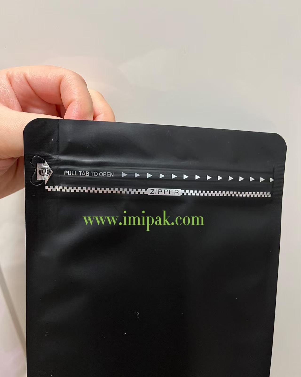 Matte black stand up pouch with pull tab zipper, shown held in hand.