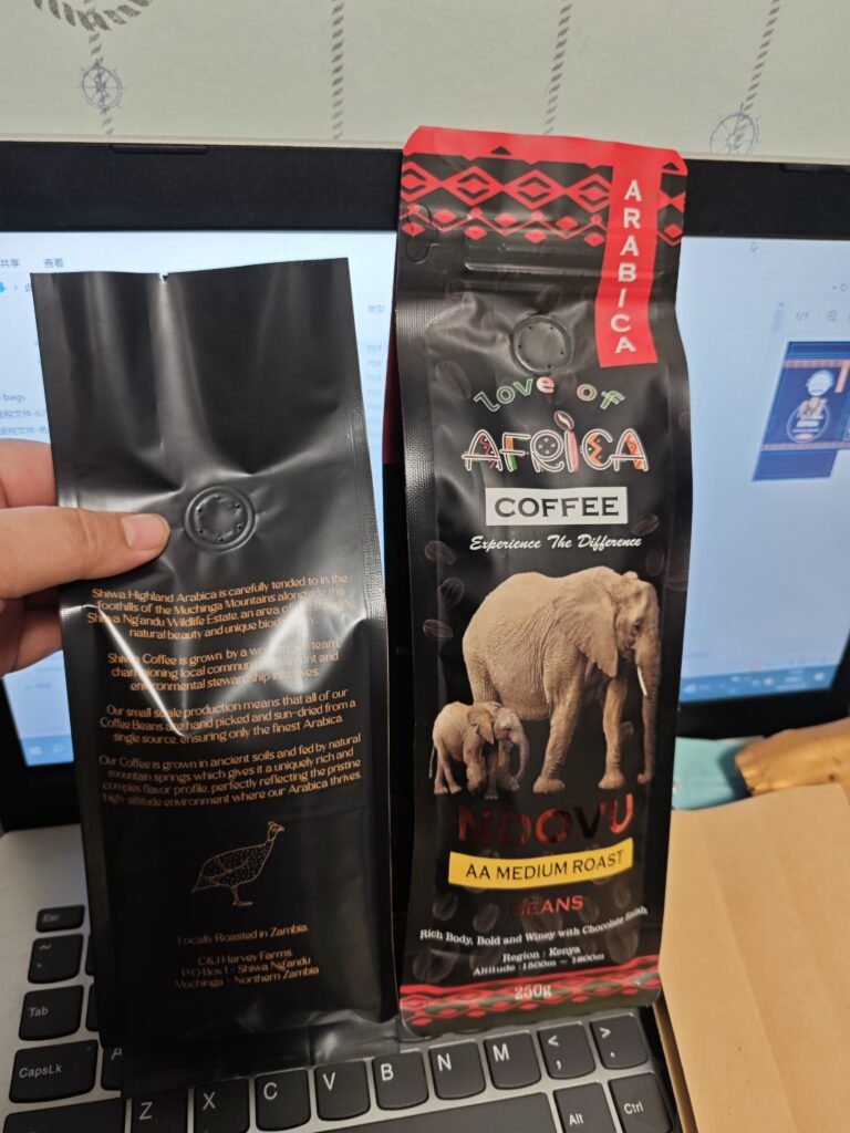 African-themed coffee bean packaging with elephant graphics, black matte finish, and bold red accents, placed on a laptop keyboard.