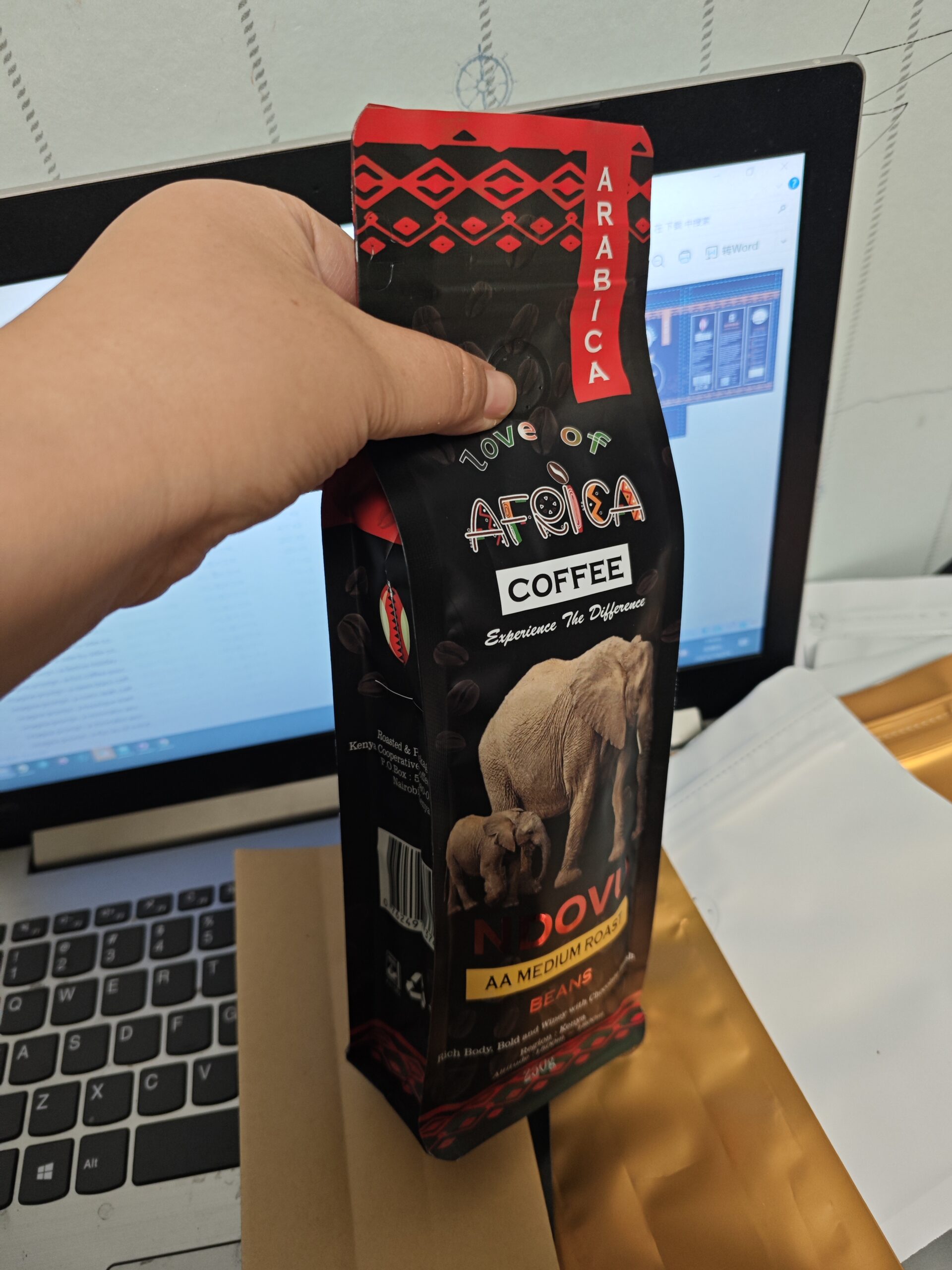 African-themed AA medium roast coffee bag with elephant design, held in hand near a laptop.