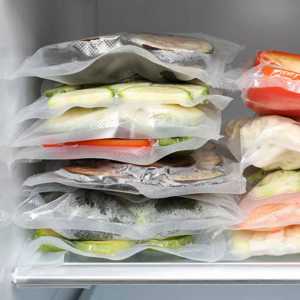 Vacuum sealed food bags with assorted vegetables neatly stacked in freezer storage.